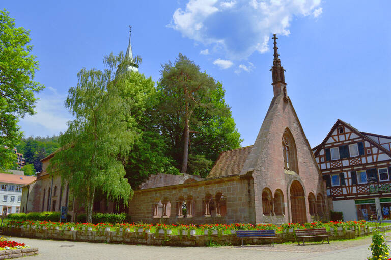 Kloster Bad Herrenalb mit einem blauen Himmel grünen Bäumen und roten Blumen im Vordergrund