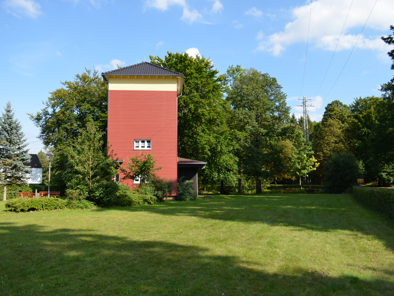 Wiese im Vordergrund, im Hintergrund ein roter Turm und blauer Himmel