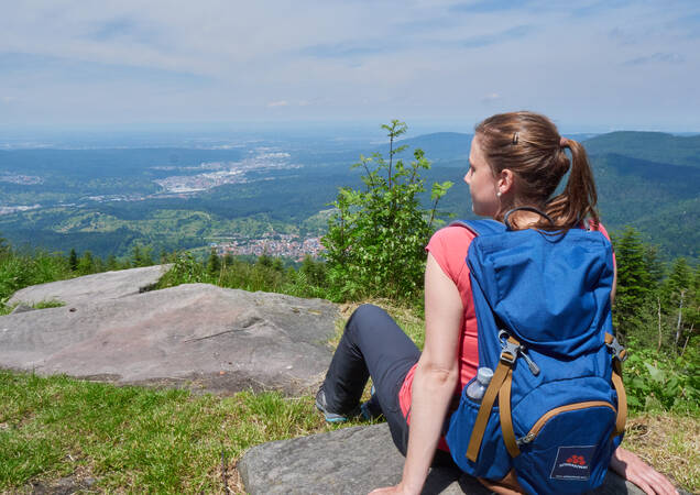 ei der Augenblick-Runde in Bad Herrenalb sitzt eine Frau auf einem großen Felsen. Sie blickt in die Ferne, umgeben von der Natur. Die Sonne scheint, und der Himmel ist strahlend blau.