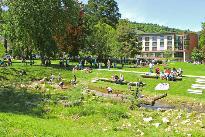 Verschiedene Personen stehen in einem Fluss oder sitzen auf Bänken im Park