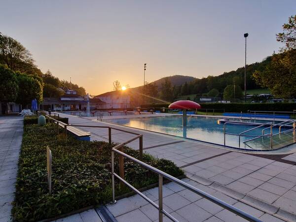 im Vordergrund ist ein leeres Schwimmbecken, im Hintergrund geht die Sonne auf