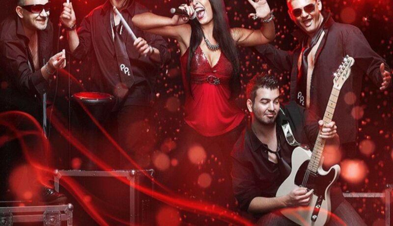 Eine Band aus fünf Mitgliedern, darunter eine Sängerin in rotem Outfit und Musiker mit Instrumenten, tritt energetisch auf einer Bühne mit roten Lichteffekten auf. | © Party Project Live
